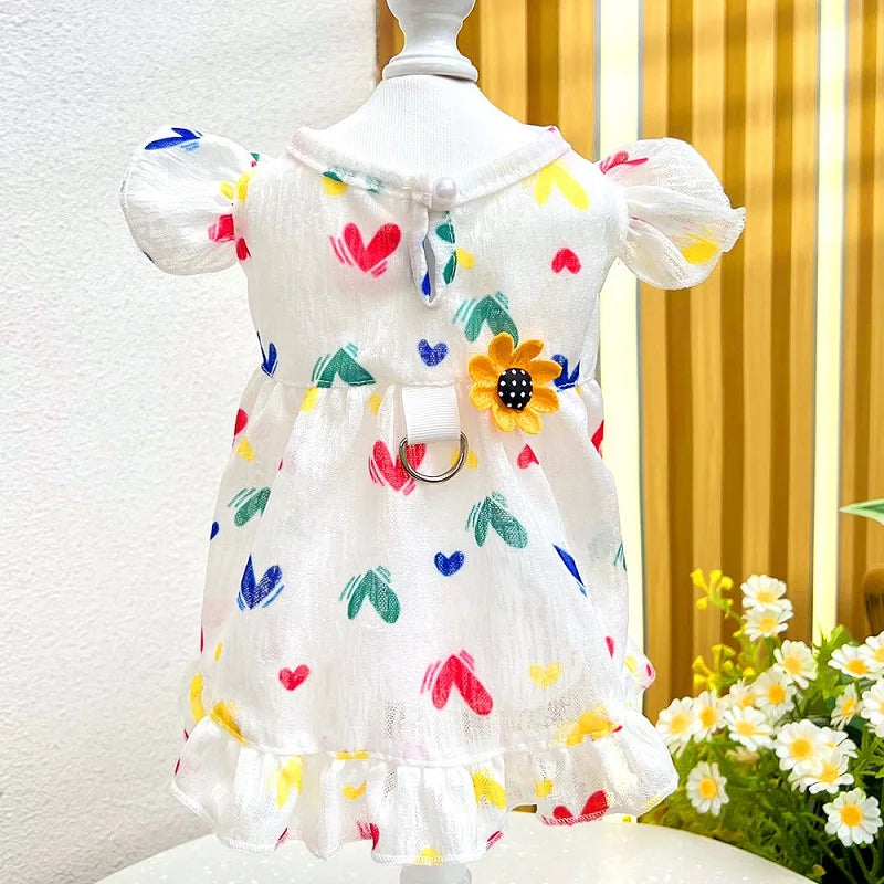 White cotton pet dress with colorful heart print and ruffled sleeves by PetoPop, featuring a yellow flower embellishment and front D-ring, displayed on mannequin.