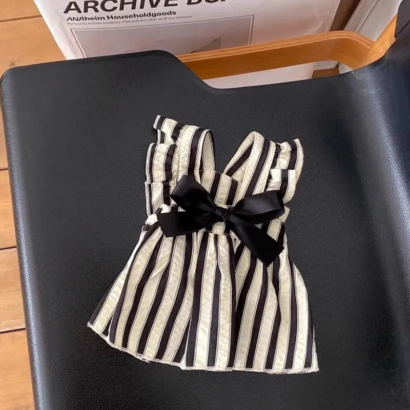 Black and white striped cotton pet dress with bow detail by PetoPop, laid flat on black surface, front view