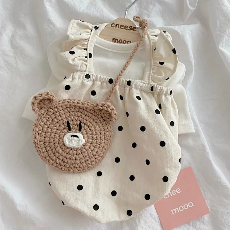 Cream polka-dot cotton pet dress by PetoPop with ruffled straps and bear-shaped crocheted bag, displayed on white fabric background